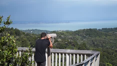 Young-caucasian-man-looking-through-lookout-binocular-at-New-Zealand-nature