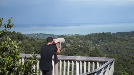 young caucasian man looking through lookout binocular at new zealand nature