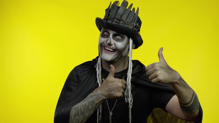 Frightening man in skeleton Halloween cosplay makeup looking at camera, showning thumbs up gesture