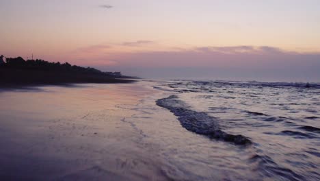 stunning colorful sunset sky reflected on water and wet sand as gentle waves roll onto a beach