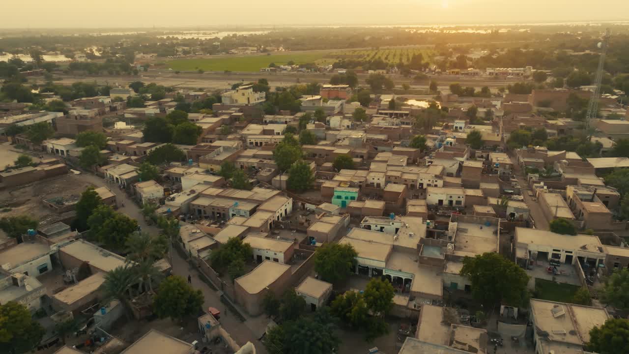 Forward drone glide over Sher Shah City village in Multan Punjab capturing the golden hazy sunlight bathing the rural houses and green fields at sunset