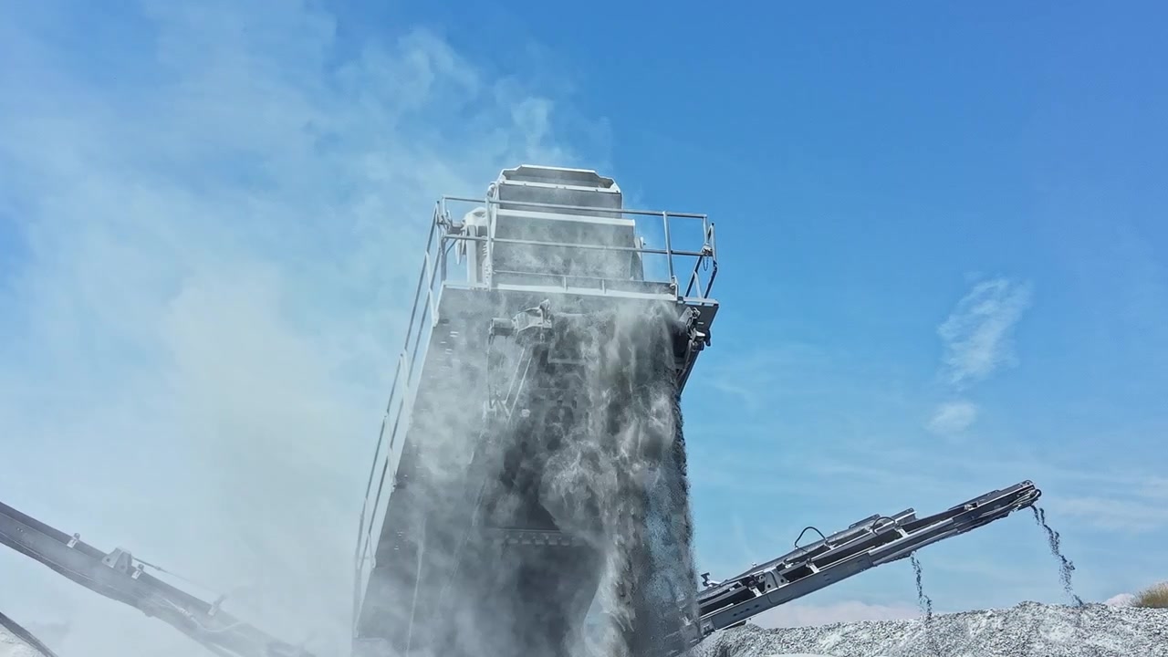 Una macchina da cava di granito opera per frantumare e lavorare materiale lapideo sotto un cielo azzurro e limpido nel pomeriggio.