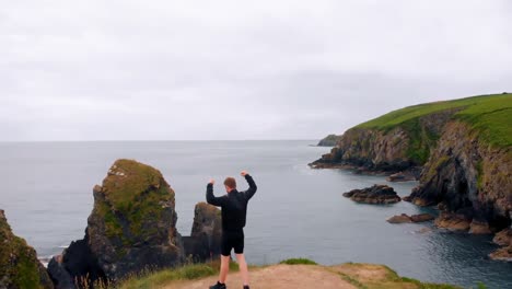 man walking on cliff with his hands spread and arms up 4k