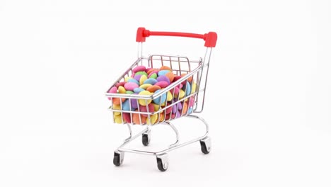 el carrito del supermercado lleno de coloridos dulces de chocolate girando en la mesa giratoria. aislado en el fondo blanco.