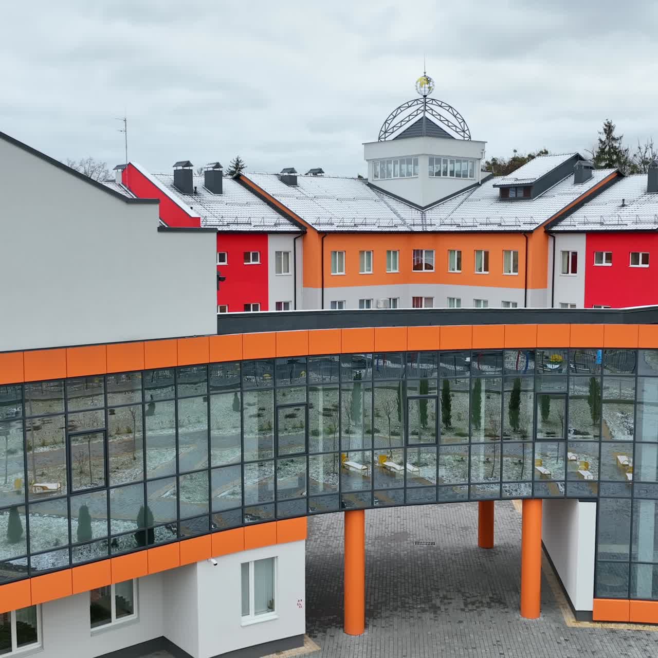 Front entrance to the building of unusual shape with mirrored windows. Beautiful new structure with courtyard. Grey sky at the backdrop