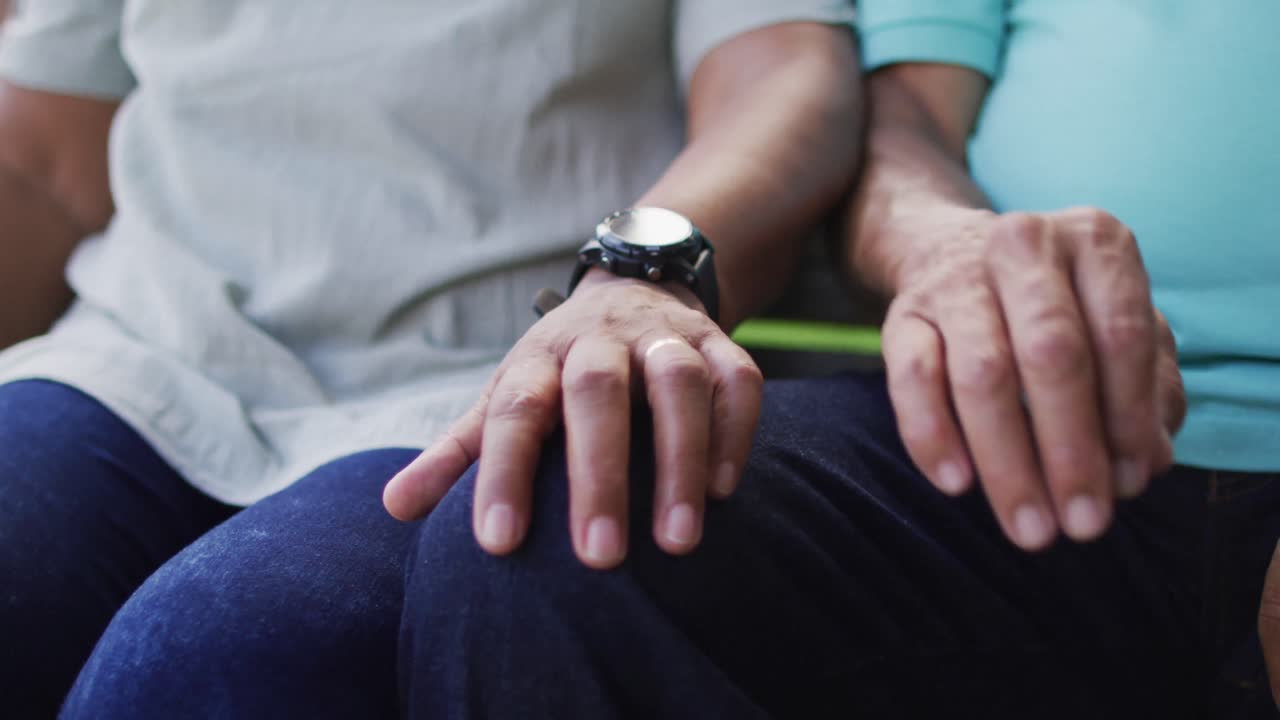 Video of midsection of biracial senior couple holding hands and sitting in garden
