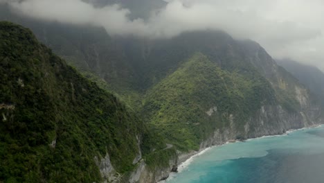 Qingshui-lush-cliffs-aerial-view-slow-tilt-up-to-cloudy-mountain-peaks-of-Taroko-gorge-Hualien-County-shoreline