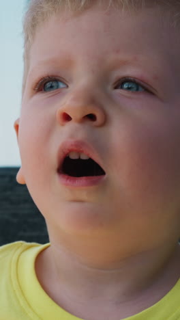 cute toddler child boy with chubby cheeks in yellow t-shirt yawns in gondola riding cable way at mountain resort close view slow motion