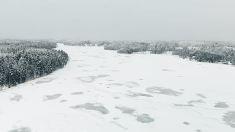 Aerial,-reverse,-drone-shot,-over-weak,-snow-covered-ice,-on-Nuuksion-Pitkajarvi,-surrounded-by-winter-forest,-on-a-overcast-day,-in-Nuuksio-national-park,-in-Espoo,-Uusimaa,-Finland