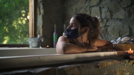 Mujer-Joven-Y-Atractiva-Que-Tiene-Un-Baño-Elegante-En-Un-Jacuzzi-Con-Máscara-Covid-Con-Una-Gran-Ventana-De-Naturaleza-Verde-Capaz-De-Cámara-Lenta-60fps