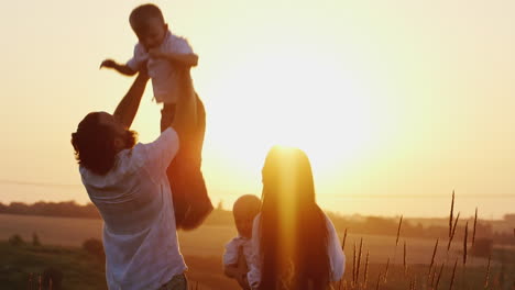 young man and woman playing with young children tosses them in the air against the sunset background