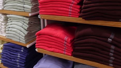 stacks of folded shirts and sweaters on wooden shelves in a clothing store