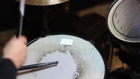 a closeup of a musician playing drums in the studio with black drum sticks