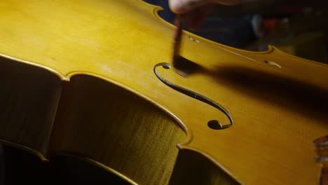 detailed close-up shows a craftsman carefully applying varnish to the top plate of a cello, highlighting the elegant curves and f-holes in a traditional cremona luthier’s workshop