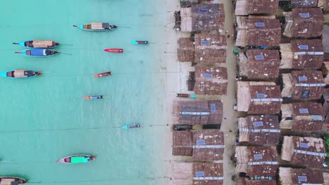 Vista-Aérea-De-Drones-De-Arriba-Hacia-Abajo-Sobre-Un-Pueblo-De-Cabañas-De-Madera-Con-Botes-De-Cola-Larga-A-Lo-Largo-De-La-Playa-En-Tailandia