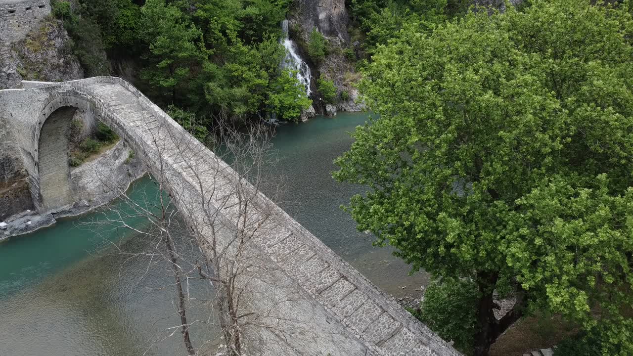 Una splendida vista laterale dello storico ponte di Konitsa, il ponte in pietra a unica arcata più grande dei Balcani. Presenta le acque color smeraldo del fiume Aoos e le lussureggianti montagne verdi dell'Epiro.