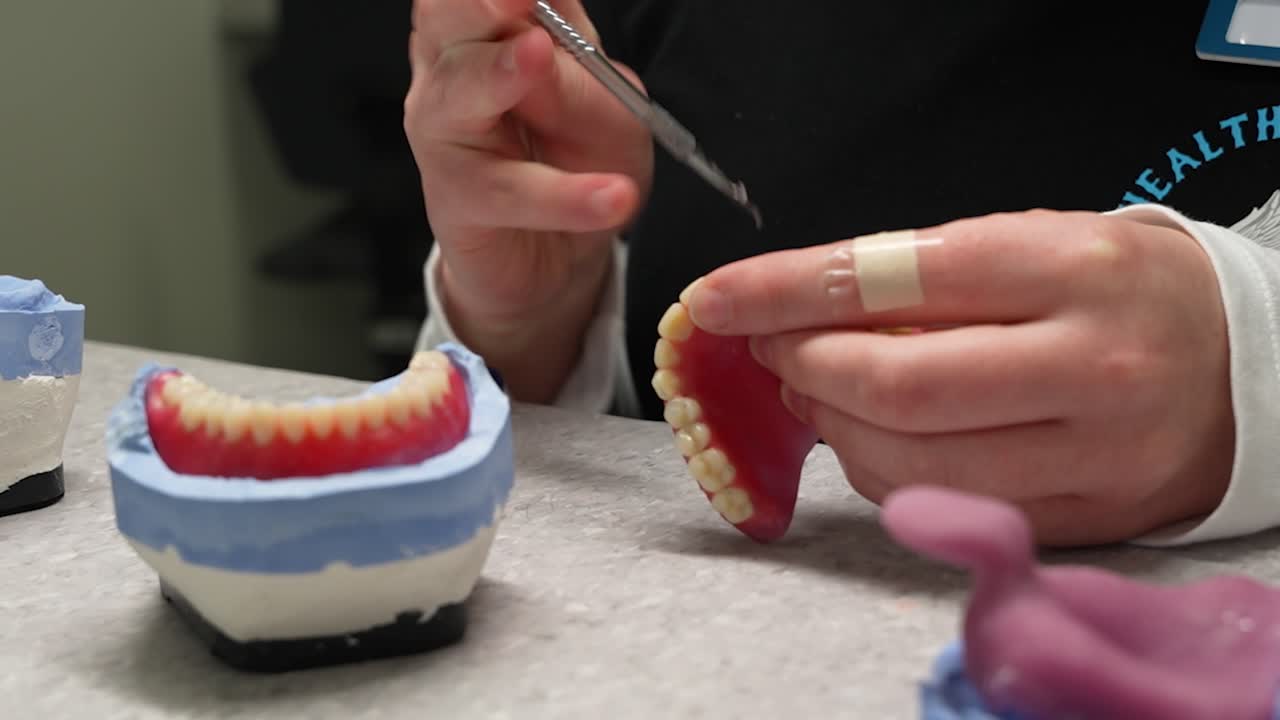 par de prótesis dentales frescas con un técnico terminando los dientes artificiales con un bisturí en un pequeño centro de salud en el taller