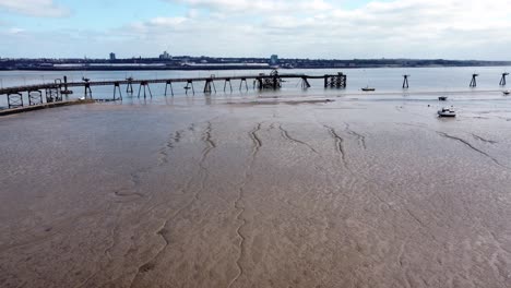 Small-fishing-boat-aerial-view-of-stranded-vessel-on-muddy-low-tide-on-Liverpool-coastline-pull-back