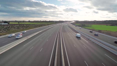 Looking-at-cars-passing-by-on-a-quiet-highway-from-above,-beautiful-horizon-with-blue-sky-and-clouds