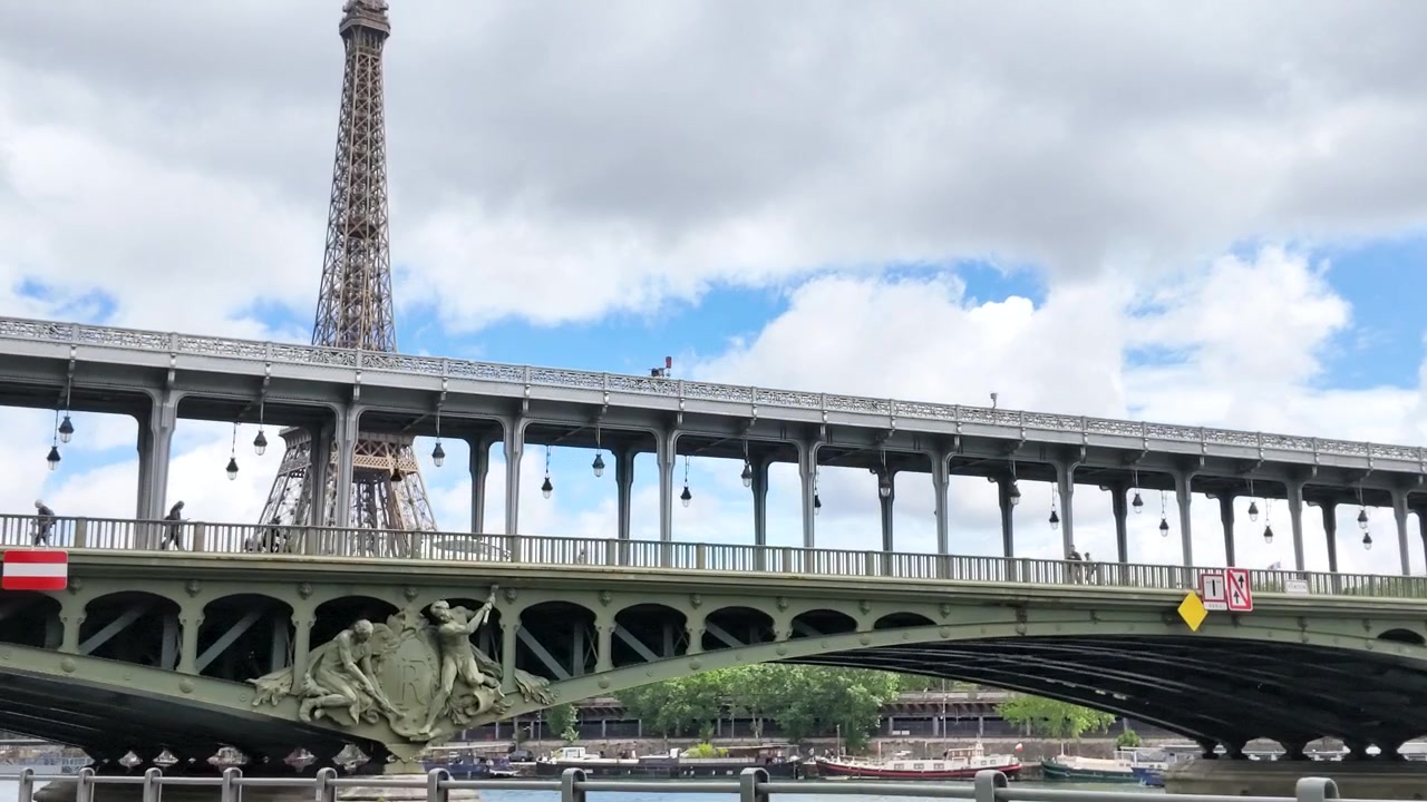 La telecamera si muove verso l'intricata struttura in acciaio del Ponte di Bir-Hakeim in una giornata nuvolosa.