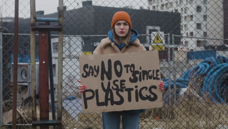 jovem ativista feminina segurando um cartaz de papelão durante um protesto contra as mudanças climáticas enquanto olha para a câmera 3