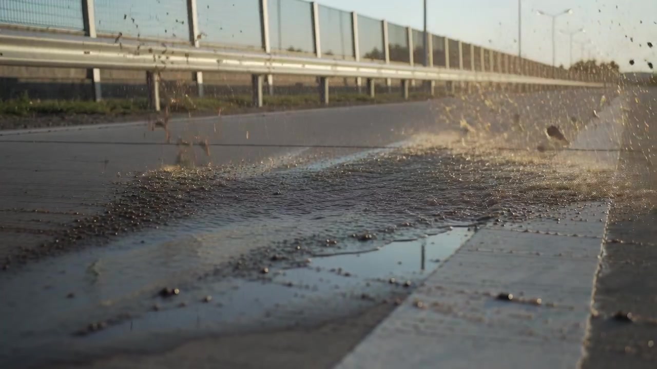 Rolling tire and wheel hub displacing puddle and gravel while driving on highway, leaving wet track