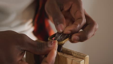 Close-up-of-hands-of-african-american-craftsman-preparing-belt-in-leather-workshop