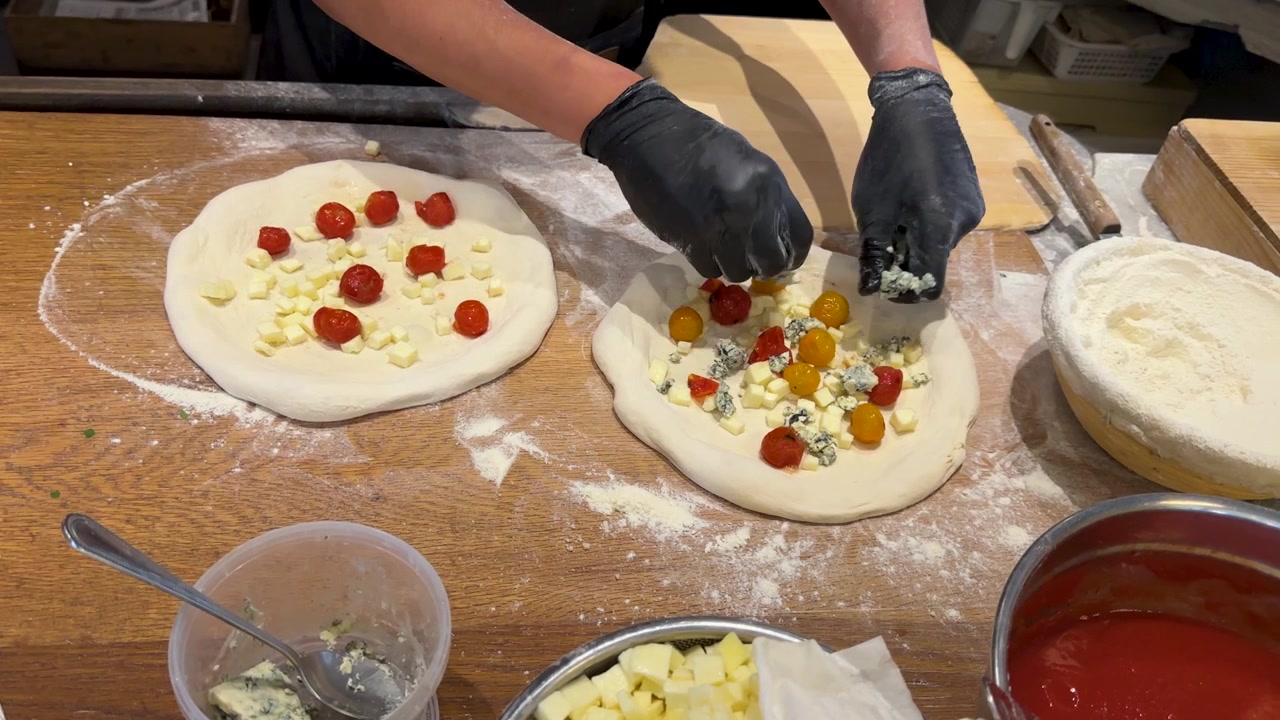 Ripresa dall'alto di uno chef che posiziona pomodorini e mozzarella sull'impasto in una cucina professionale