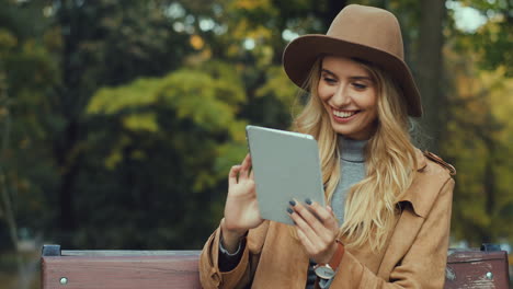 caucasian blonde caucasian woman sitting on the bench and using a tablet in the park in autumn