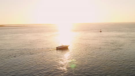 aerial of a small jet boat pleasure cruising in a calm sunset lit ocean