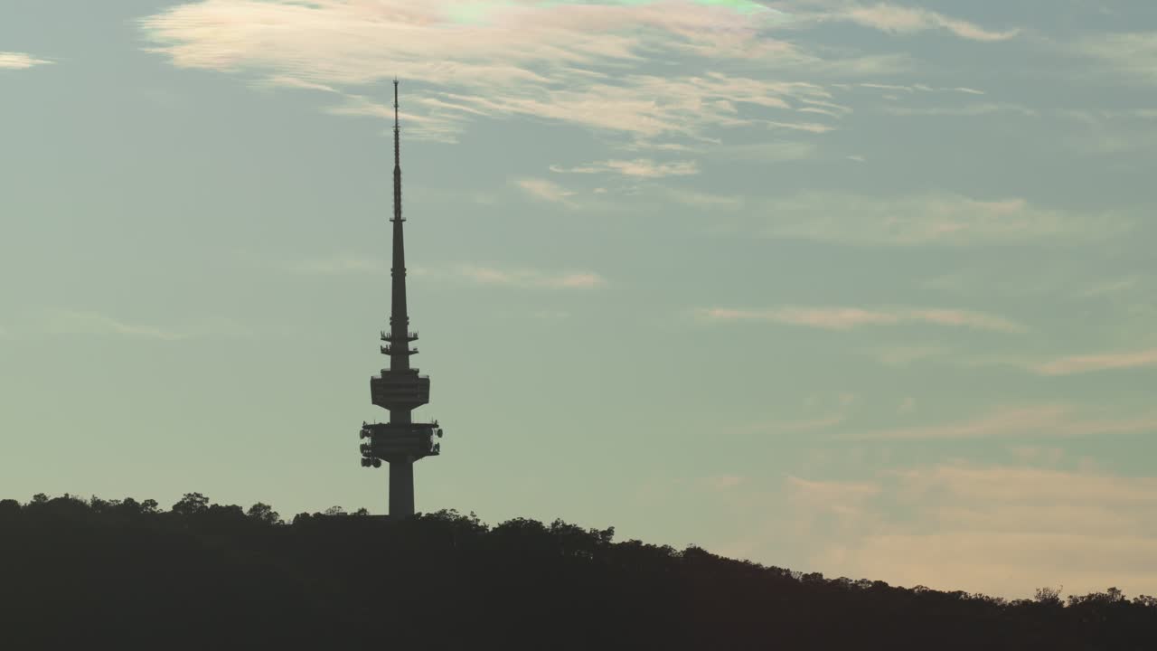 A mid shot of the Canberra Tower during sunrise, silhouetted against the blue sky and softly lit with early warmth