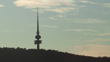 a mid shot of the canberra tower during sunrise, silhouetted against the blue sky and softly lit with early warmth