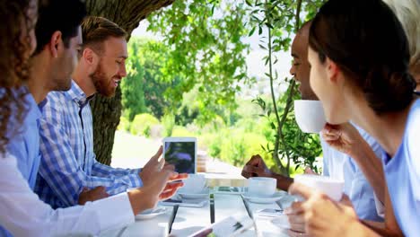 Grupo-De-Amigos-Discutiendo-Sobre-Una-Tableta-Digital-En-Una-Cafetería-Al-Aire-Libre