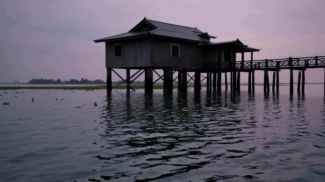 Tranquil waters reflect a serene wooden pier house at dusk, showcasing the peaceful ambiance and natural beauty of the surrounding landscape in a continuous motion sequence