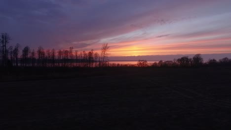 Lake-Burtnieks-in-late-autumn-red-sky-sunset-aerial-wide-view-wit-tree-silhouette