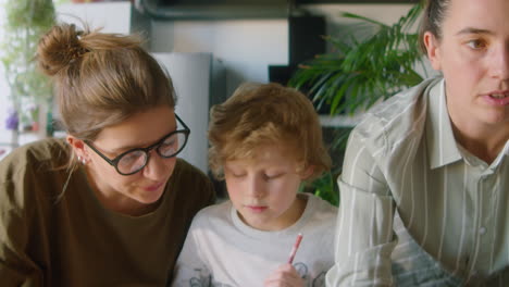 kid doing homework with assistance of lesbian mothers
