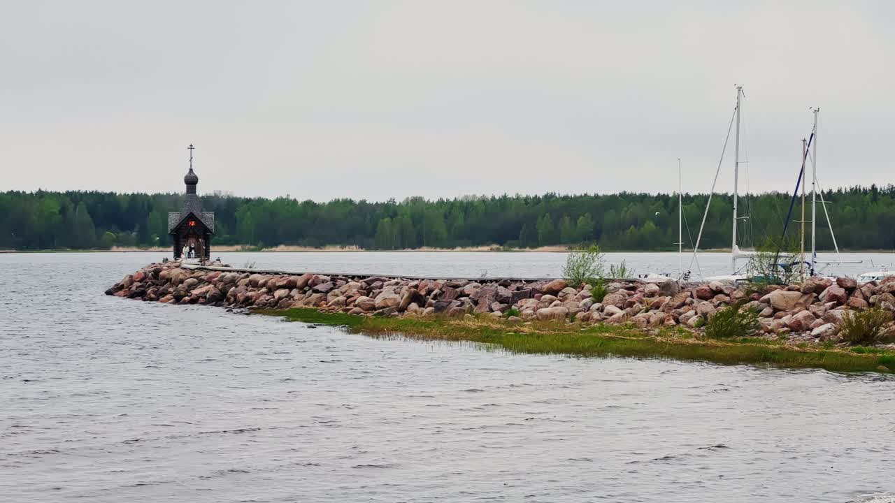 старая часовня стоит на каменном мысе на воде в ленинградской области россии в облачную погоду, лес на заднем плане