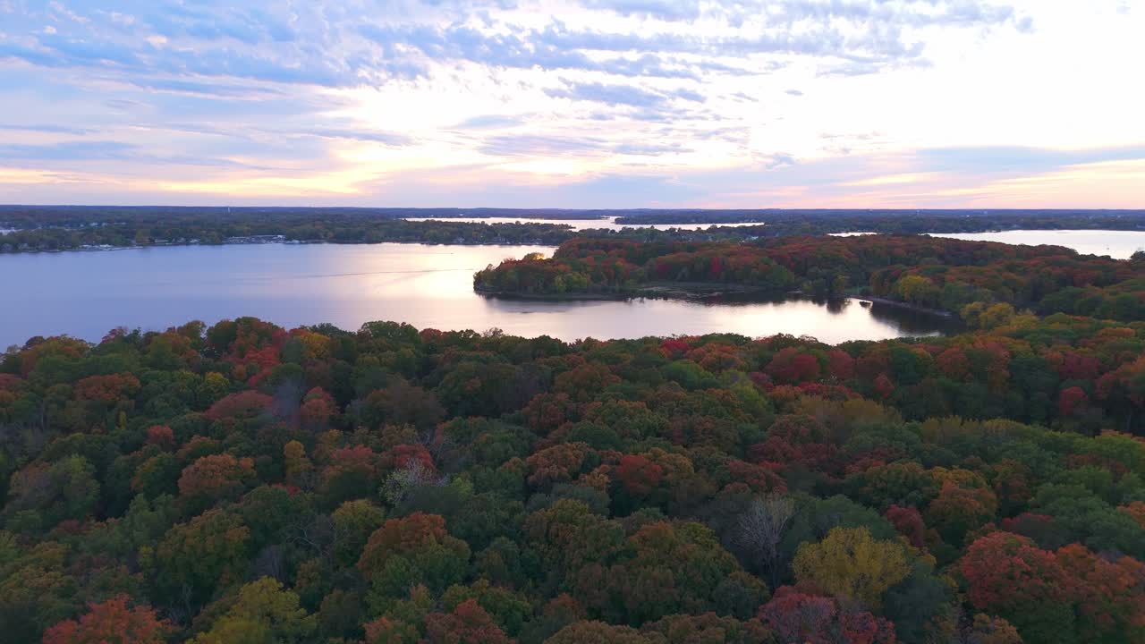 An aerial view of Lake Minnetonka reveals a shoreline ablaze with autumn colors, as fiery reds, golden yellows, and deep oranges dominate the surrounding trees