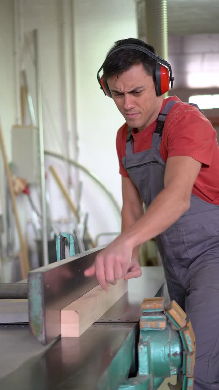 A man operating a woodworking machine in a workshop, wearing ear protection