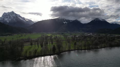 sunlight breaks between clouds casting bright rays on farm fields along shoreline of lake