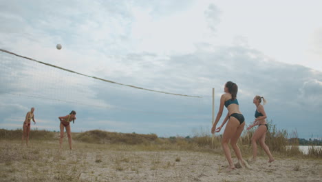 women players are playing match of beach volleyball at summer one team is attacking and player of other is blocking ball