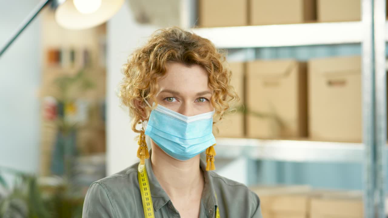 vista de cerca de una diseñadora caucásica con máscara médica mirando la cámara en el almacén de la tienda de ropa