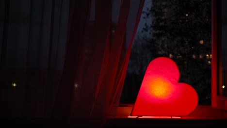 luz nocturna en forma de corazón roja junto a la ventana por la noche