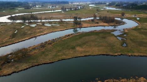 Aerial-footage-of-flooded-fields-in-the-countryside,-with-a-meandering-river-and-sun-reflections-on-the-water