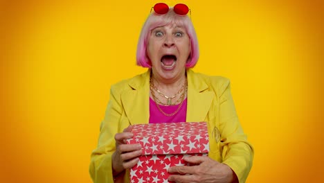 amazed senior grandmother woman opening gift box and smiling joyfully, satisfied with nice present