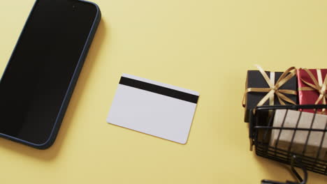 video de un teléfono inteligente con pantalla en blanco, tarjeta de crédito, carrito de compras sobre fondo amarillo