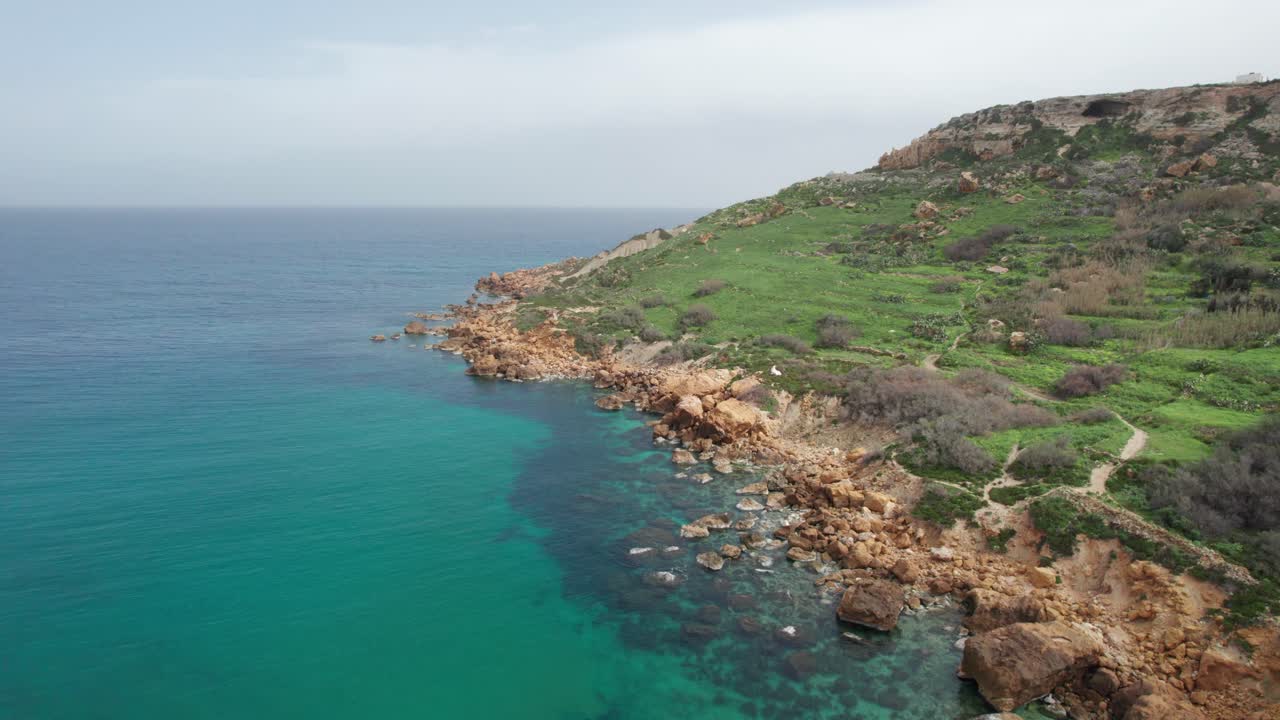 volando sobre una costa rocosa naranja con agua turquesa en la base de una colina verde