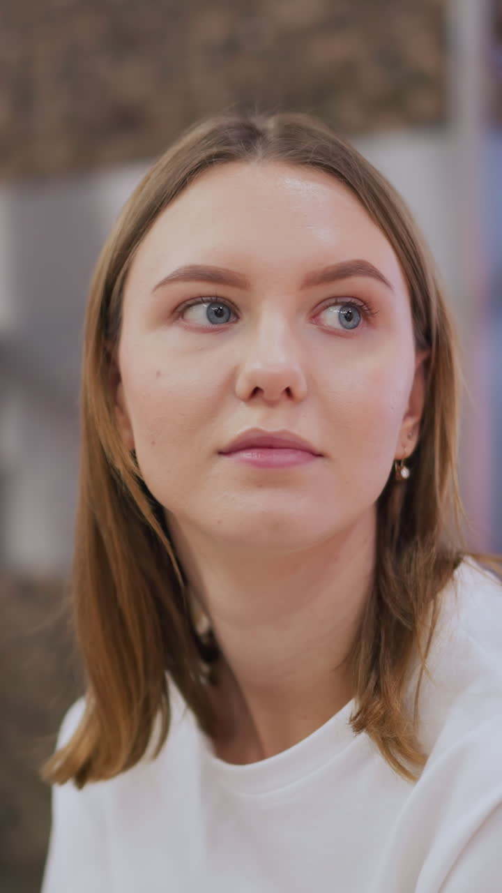 mujer joven sentada en el interior con una mirada contemplativa, rodeada de sutiles reflejos de luz azul y tonos cálidos en un espacio moderno