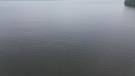 Flying-Above-Calm-Waters-Of-A-Lake-On-A-Cloudy-Day---drone-shot