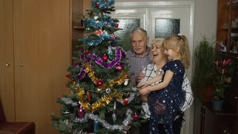 Kid-with-senior-grandmother-and-grandfather-decorating-artificial-Christmas-tree,-lights-garlands